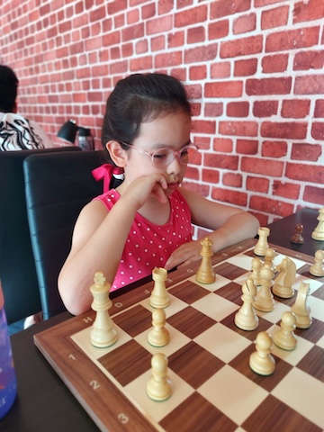 Small girl playing chess at the Red Knight Chess Club in Bangkok.