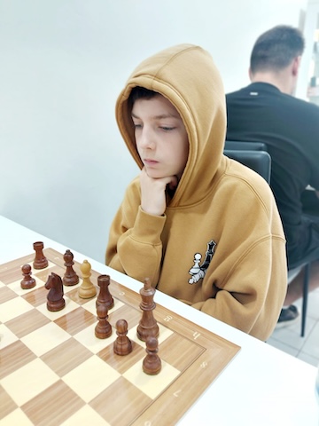 Boy in hoodie playing chess at the Red Knight Chess Club in Bangkok.